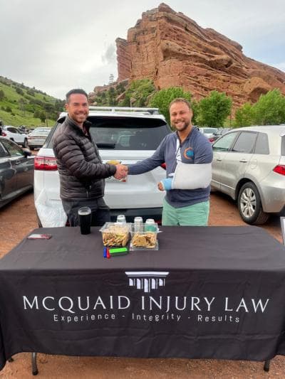 Brendan McQuaid shaking hands with a client whose arm is in a sling, at a McQuaid Injury Law table with red rock formations behind